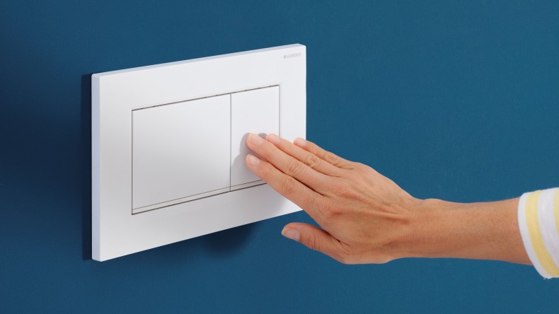 A hand activates the flush on a white Sigma20 actuator plate (© Geberit)